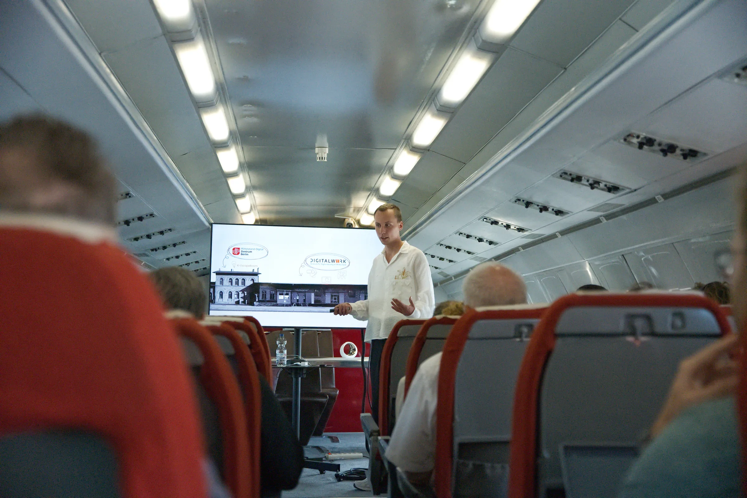 Jonathan Grießl präsentiert beim Mittelstand-Digital Zentrum Berlin in einem zum Konferenzraum umgebauten Flugzeug